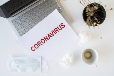 Coronavirus ve karantina yüzünden ofiste hasta bir çalışanın terkedilmiş işyeri. Tıbbi maske, peçete ve bir fincan bitmiş kahve ile birlikte. Dünya çapında salgın konsepti