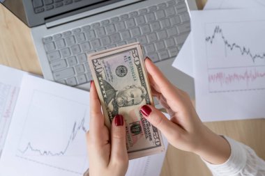 Kadın serbest çalışan elinde 50 Amerikan doları tutuyor ve kârı ve geliri sayıyor. Ofis masasındaki kağıda grafikler ve çizelgeler basılmış. Düz yatıyordu