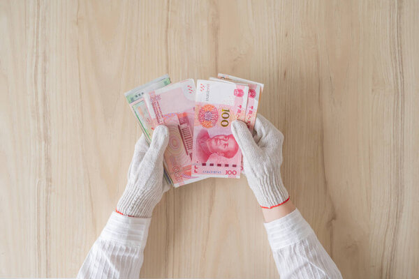 Chinese female hand in protective from coronavirus (virus) gloves counting money of south-east Asia. China yuan (CNY) Currency of Hong Kong, Indonesia, Malaysia, Thai, Singapore dollar.