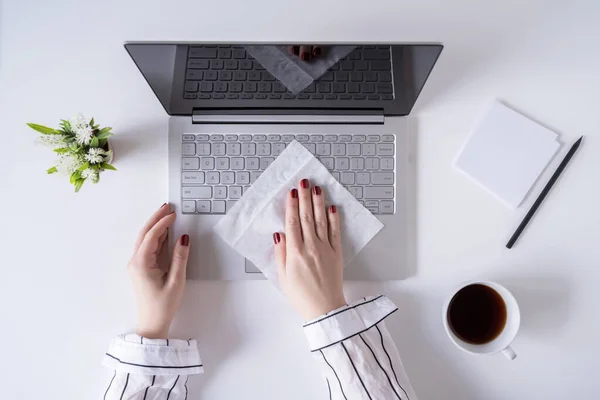 A woman worker cleaning with antivirus wet wipe a laptop and a working office desk before starting work for protect herself from bacteria and virus.