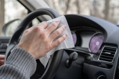Adam kendini bakteri ve virüsten korumak için antivirüs antibakteriyel ıslak mendil (peçete) kullanarak arabanın direksiyon simidini temizliyor..