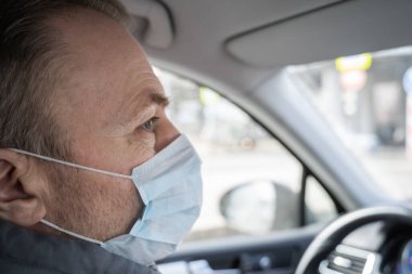 Kendini araba kullanan bakteri ve virüsten korumak için maske takan orta yaşlı bir adamın yüzü. Coronavirus. Salgın
