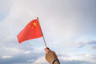 Gün batımında sallanan Çin bayrağı taşıyan kadın eli. Kavram