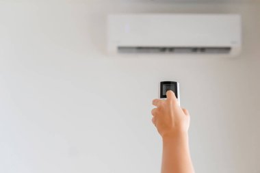 Kumral kadın odanın içinde klimadan uzaktan kumanda tutuyor. Arka plan.