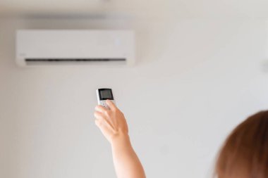 Kumral kadın odanın içinde klimadan uzaktan kumanda tutuyor. Arka plan.