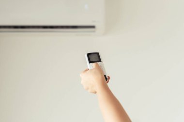 Kumral kadın odanın içinde klimadan uzaktan kumanda tutuyor. Arka plan.