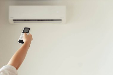 Kumral kadın odanın içinde klimadan uzaktan kumanda tutuyor. Arka plan.
