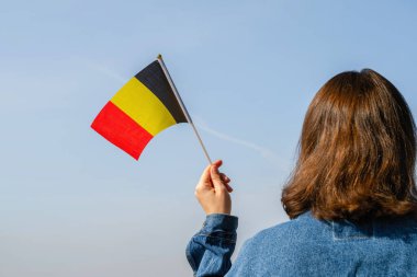 Mavi gökyüzünde sallanan Belçika bayrağı taşıyan bir kadın eli. Belçika. Kavram