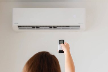 Kumral kadın odanın içinde klimadan uzaktan kumanda tutuyor. Arka plan.