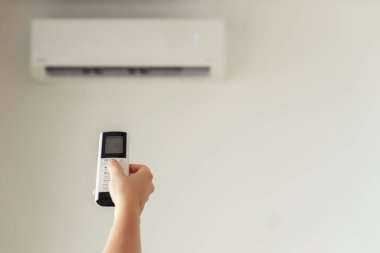 Kumral kadın odanın içinde klimadan uzaktan kumanda tutuyor. Arka plan.