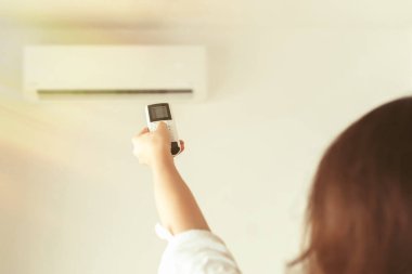 Kumral kadın odanın içinde klimadan uzaktan kumanda tutuyor. Arka plan.