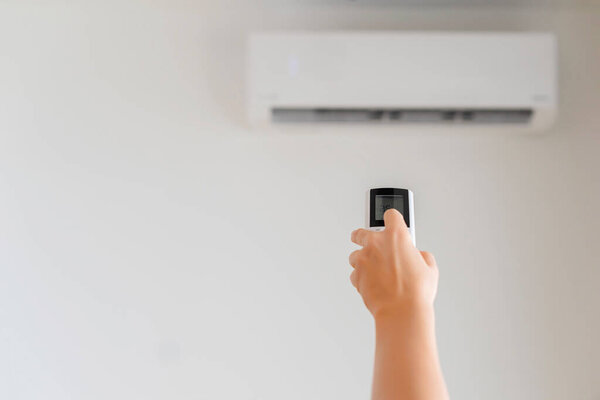 Brunette woman holding remote controller from air conditioner inside the room. Back view.