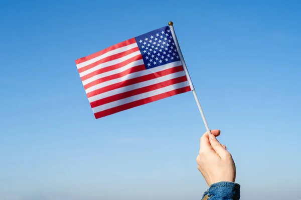 Woman hand with American swaying flag on the blue sky. America. USA. Concept