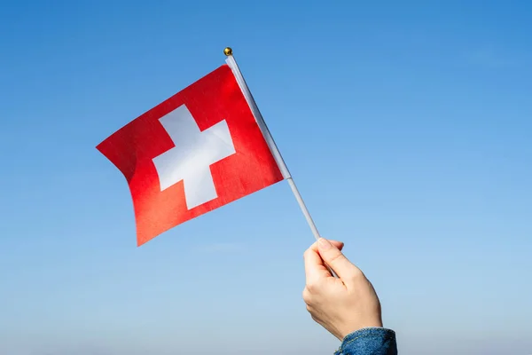 Woman hand with Swiss swaying flag on the blue sky. Switzerland. Concept