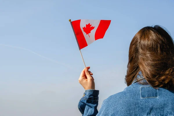 Woman hand with Canada swaying flag on the blue sky. America. USA. Concept
