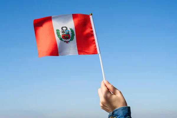Woman hand with Peru swaying flag on the blue sky. South America. Concept