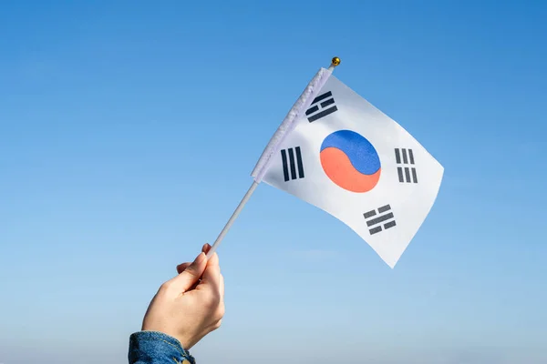 Woman hand with South Korea swaying flag on the blue sky. Concept