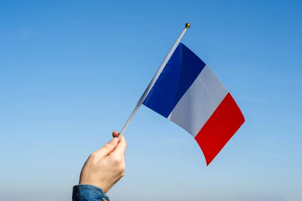 Woman hand with French swaying flag on the blue sky. France. Concept