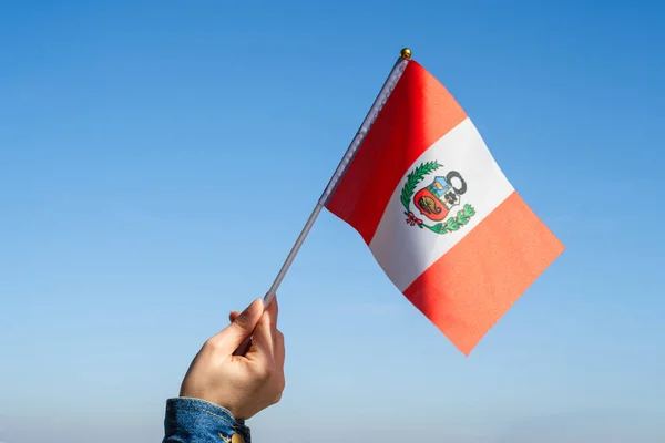 Woman hand with Peru swaying flag on the blue sky. South America. Concept
