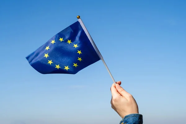 Woman hand with EU(European) swaying flag on the blue sky. Europe. Concept