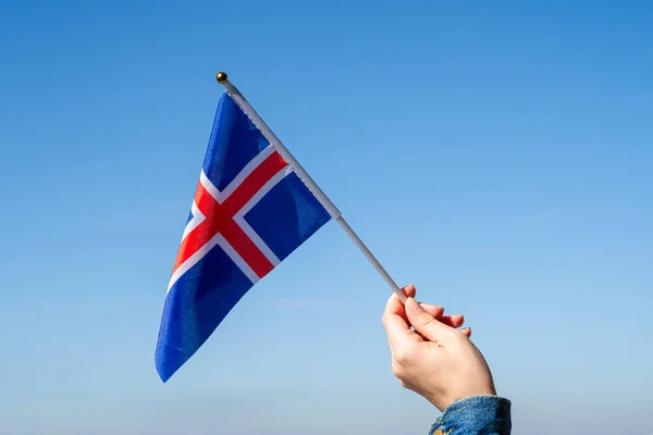 Woman hand with Iceland swaying flag on the blue sky. Concept