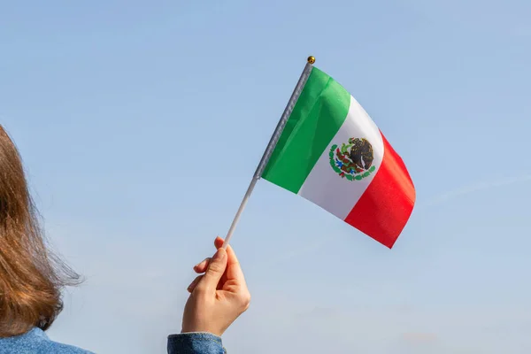 Woman hand with Mexico swaying flag on the blue sky. North America. Concept