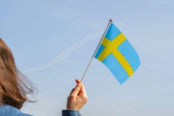 Woman hand with Swedish swaying flag on the blue sky. Sweden. Concept