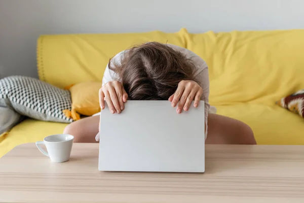 Woman freelancer clasped head by hand sitting on the couch with laptop and and worried about bad news. Work at home. Concept.