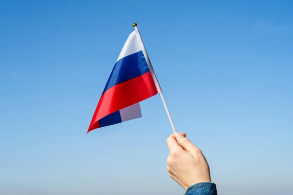 Woman hand with Russian swaying flag on the blue sky. Russia. Concept