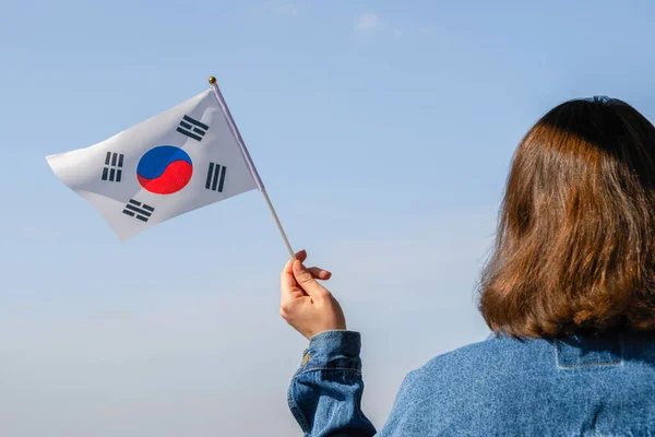 Woman hand with South Korea swaying flag on the blue sky. Concept