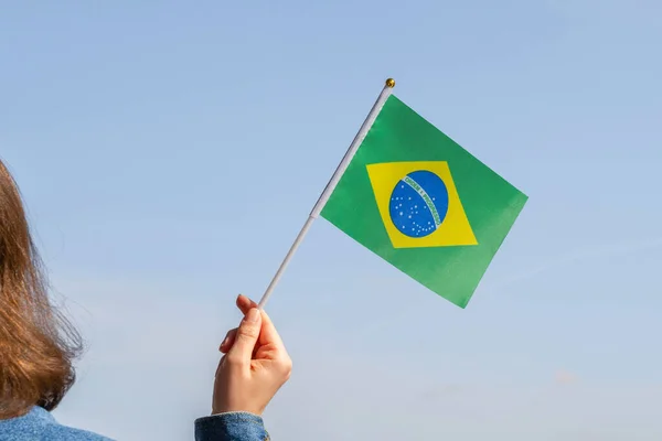 Woman hand with Brazil swaying flag on the blue sky. South America. Concept