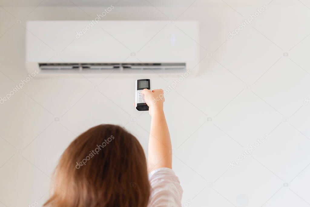 Brunette woman holding remote controller from air conditioner inside the room. Back view.