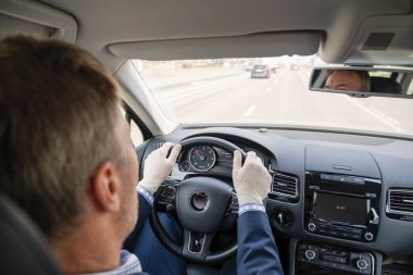 Mavi takım elbiseli orta yaşlı bir işadamı ve kendini araba kullanan bakteri ve virüsten korumak için lastik eldivenler. Coronavirus. Salgın.