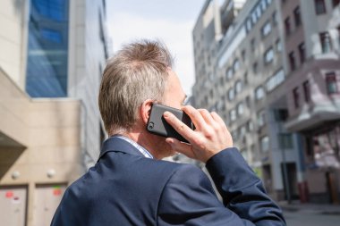 Yalnız, orta yaşlı, gri saçlı, mavi takım elbiseli bir işadamı. Telefonla arıyor. Boş şehir caddesinde duruyor..