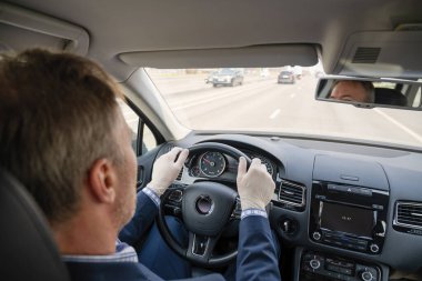 Mavi takım elbiseli orta yaşlı bir işadamı ve kendini araba kullanan bakteri ve virüsten korumak için lastik eldivenler. Coronavirus. Salgın.