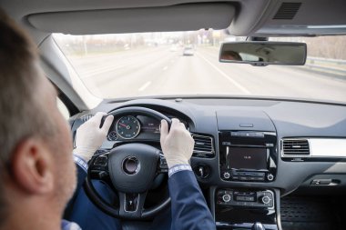 Mavi takım elbiseli orta yaşlı bir işadamı ve kendini araba kullanan bakteri ve virüsten korumak için lastik eldivenler. Coronavirus. Salgın.