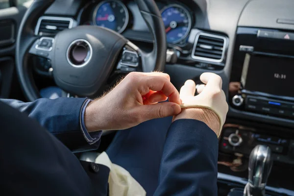 青いスーツの中世のビジネスマンは車を運転している間細菌及びウイルスから身を守るためのゴム手袋を置く コロナウイルス パンデミック — ストック写真