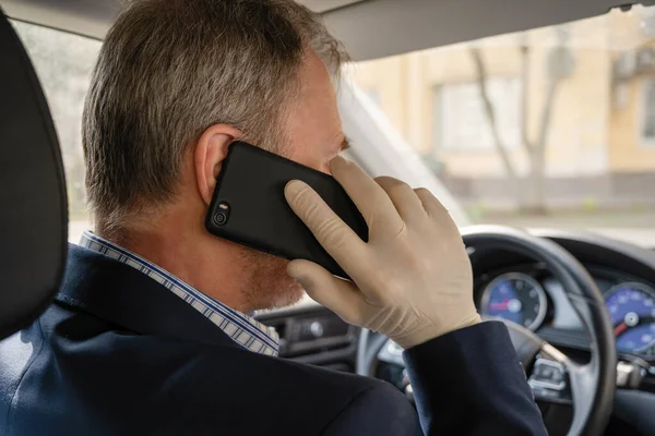 middle aged man calling on the phone in rubber gloves while driving a car. protection from bacteria and virus while driving a car.