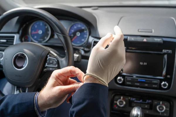 青いスーツの中世のビジネスマンは車を運転している間細菌及びウイルスから身を守るためのゴム手袋を置く コロナウイルス パンデミック — ストック写真