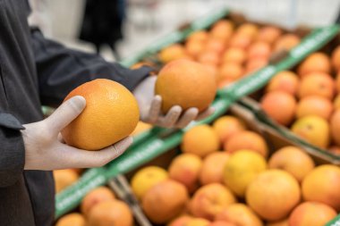Süpermarkette greyfurt (meyve) alan koruyucu lastik eldivenli bir müşteri. Coronavirus salgını sırasında bakteri ve virüsten korunma. 
