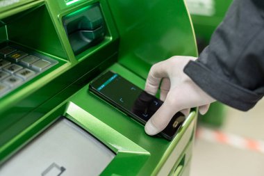 Korunaklı lastik eldivenleri teslim eden adamlar, NFC terminalinde Coronavirus 'a karşı ATM' den cep telefonuyla para çekiyorlar. Salgın. 