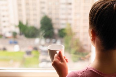 Yalnız bir genç kadının evinin penceresinde dikilirkenki görüntüsü. Kız sabahın köründe kahve içer..