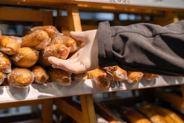 Koruyucu lastik eldivenli bir adam markette, süpermarkette ekmek seçiyor. Coronavirus salgını sırasında bakteri ve virüsten korunma. daha az güvenli teslimat