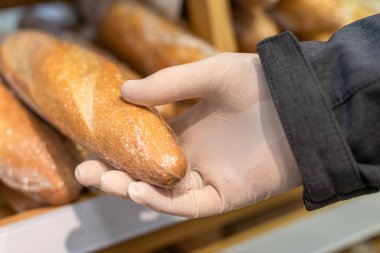 Koruyucu lastik eldivenli bir adam markette, süpermarkette ekmek seçiyor. Coronavirus salgını sırasında bakteri ve virüsten korunma. daha az güvenli teslimat