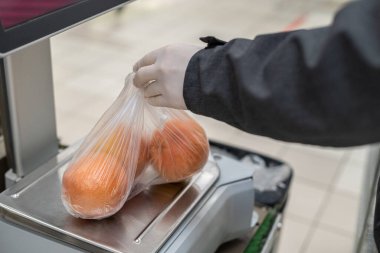 Plastik torbaya portakal koyan koruyucu lastik eldivenli adam süpermarkette teraziye koyuyor. Bakteri ve virüsten korunma. Salgın. Koronavirüs. 