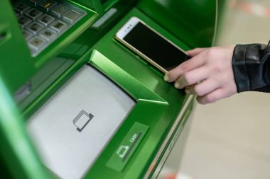 Bir kadın cep telefonuyla ATM 'den para çekiyor bir NFC terminali