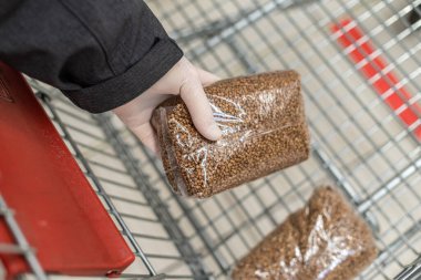Virüs salgını sırasında alışveriş. Koruyucu lastik eldivenli bir müşteri bir paket karabuğday koyarak alışveriş arabasına bir paket karabuğday koyar. Market, süpermarket. Salgın. Koronavirüs. 