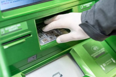 Erkekler, koronavirüs salgını sırasında para çekmek için bankanın klavyesine bir PIN kodu yerleştirmek amacıyla koruyucu lastik eldivenler veriyorlar. Salgın. 