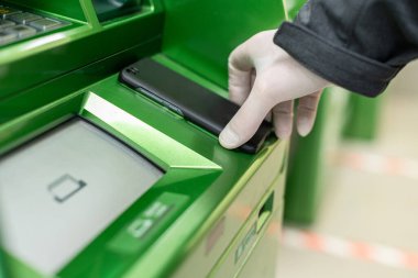 Korunaklı lastik eldivenleri teslim eden adamlar, NFC terminalinde Coronavirus 'a karşı ATM' den cep telefonuyla para çekiyorlar. Salgın. 