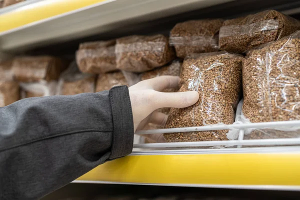 Virüs salgını sırasında alışveriş. Koruyucu lastik eldivenli bir müşteri süpermarketten bir paket karabuğday alıyor. Salgın. Koronavirüs. 